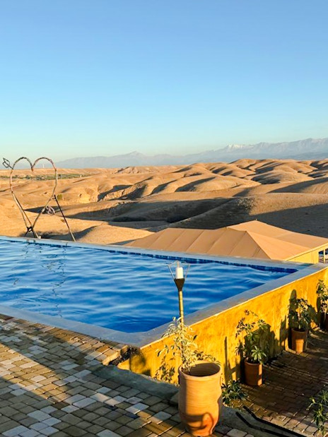 Infinity pool overlooking Agafay Desert near Marrakesh with distant mountains.