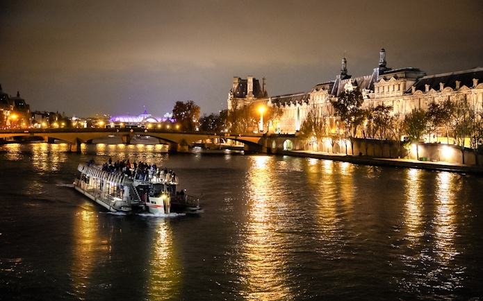 Cruise boat on Seine River at night with illuminated Parisian buildings.