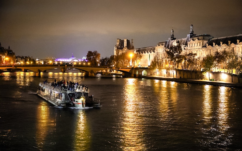 Cruise boat on Seine River at night with illuminated Parisian buildings.