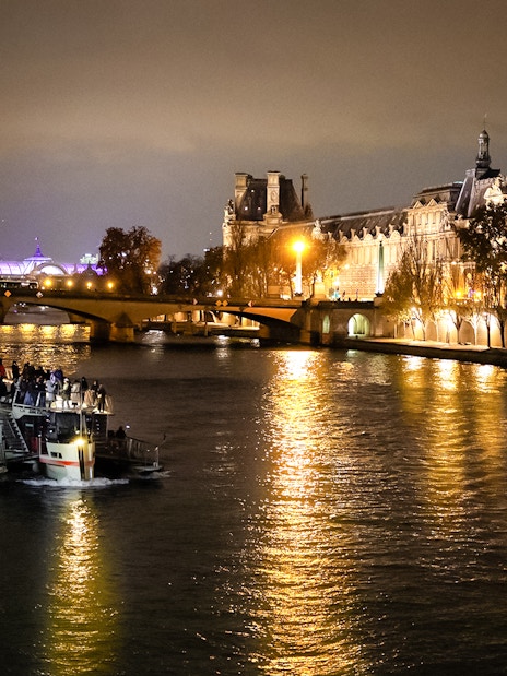 Cruise boat on Seine River at night with illuminated Parisian buildings.