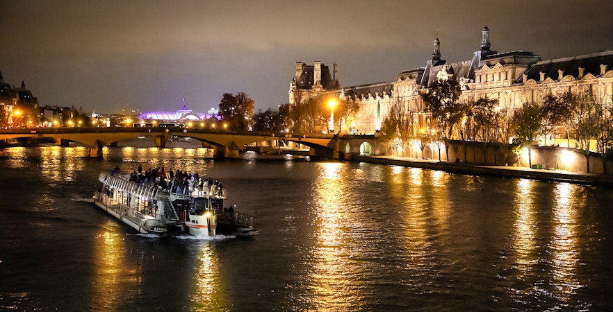 Cruise boat on Seine River at night with illuminated Parisian buildings.
