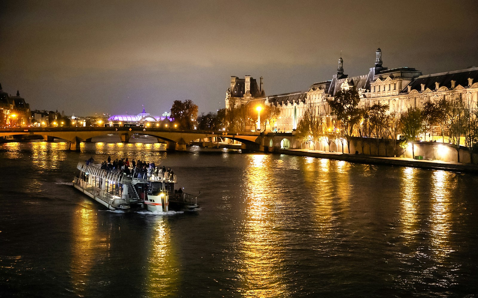 Cruise boat on Seine River at night with illuminated Parisian buildings.
