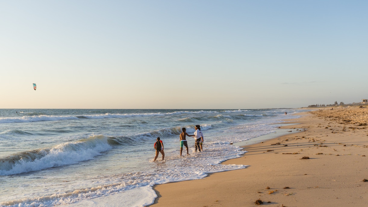 Young children having an adventure and playing in the shallow waves on the beach in the evening sunset at Scarborough beach, Perth
