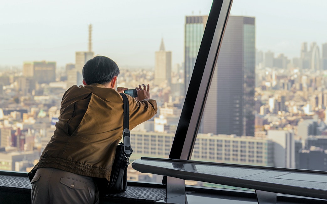 Tourist photographing Tokyo skyline from Tokyo Tower observation deck.