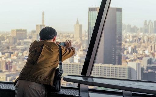 Tourist photographing Tokyo skyline from Tokyo Tower observation deck.