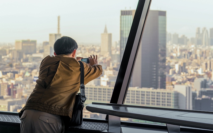 Tourist photographing Tokyo skyline from Tokyo Tower observation deck.