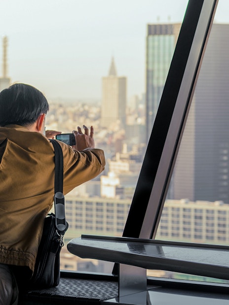 Tourist photographing Tokyo skyline from Tokyo Tower observation deck.