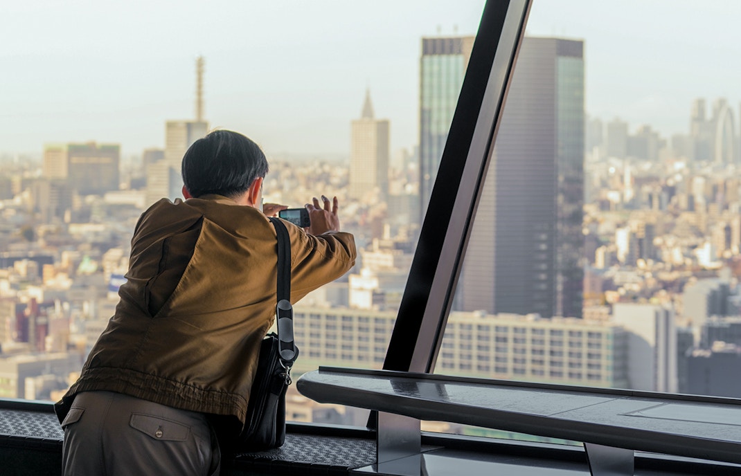 Tourist capturing cityscape from Tokyo Tower observation deck, Japan.