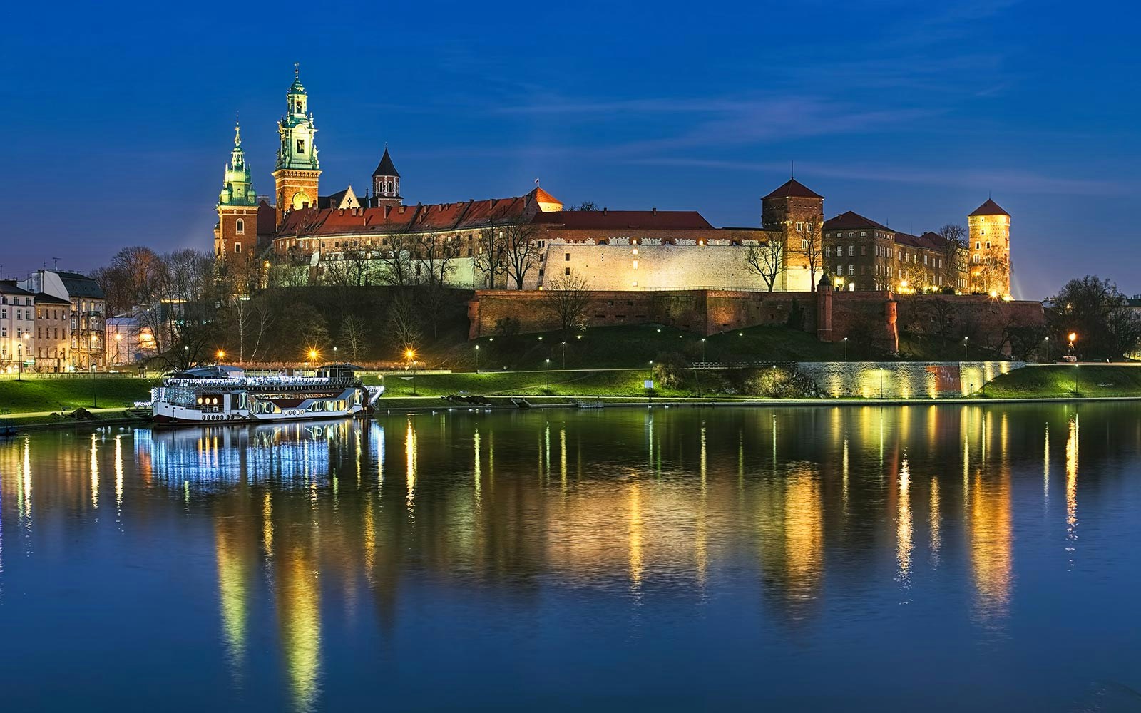 Vistula River night cruise with illuminated Krakow skyline and historic buildings in view.