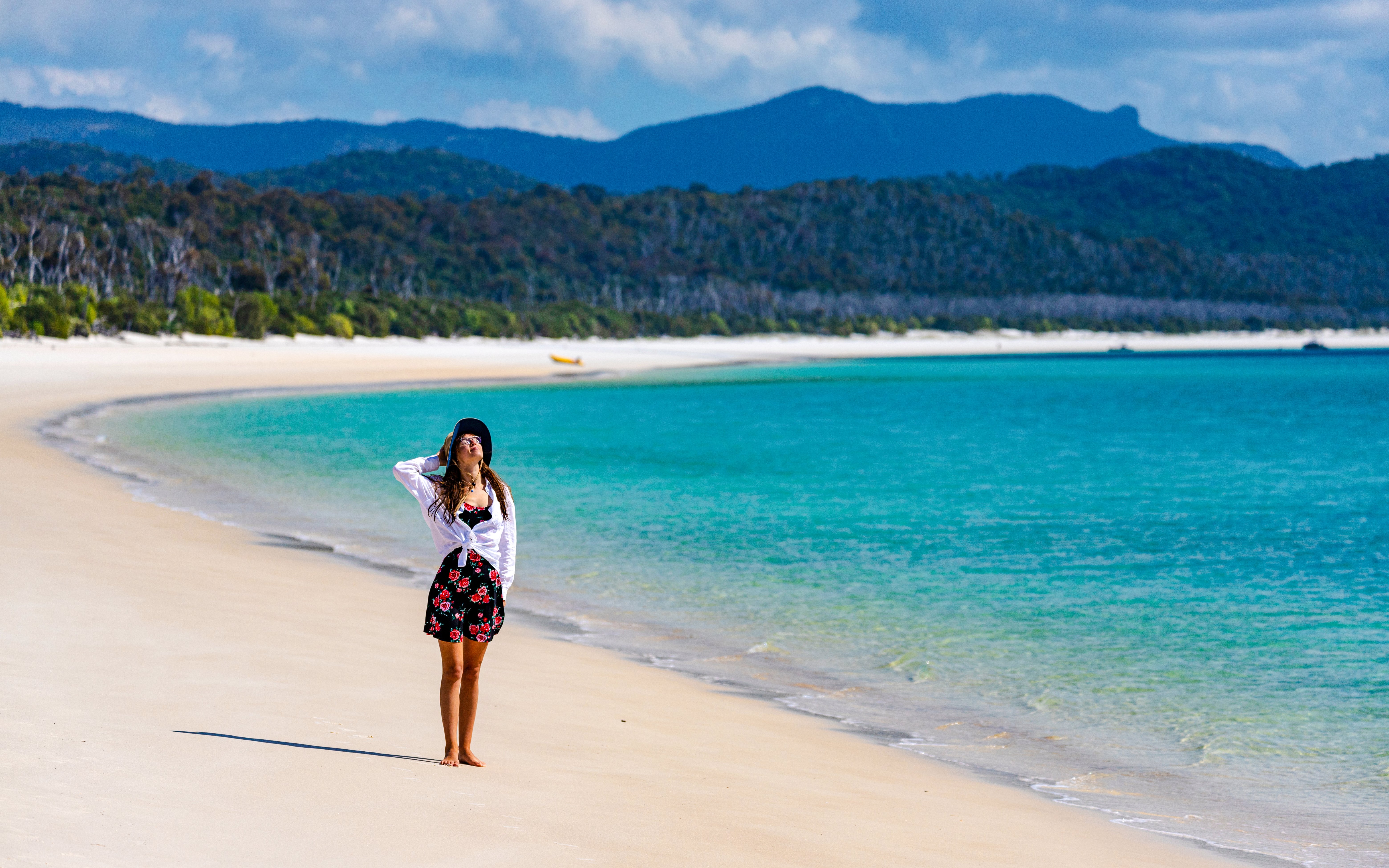 Person standing on Whitehaven Beach, Whitsunday Island, with turquoise water and forested hills.