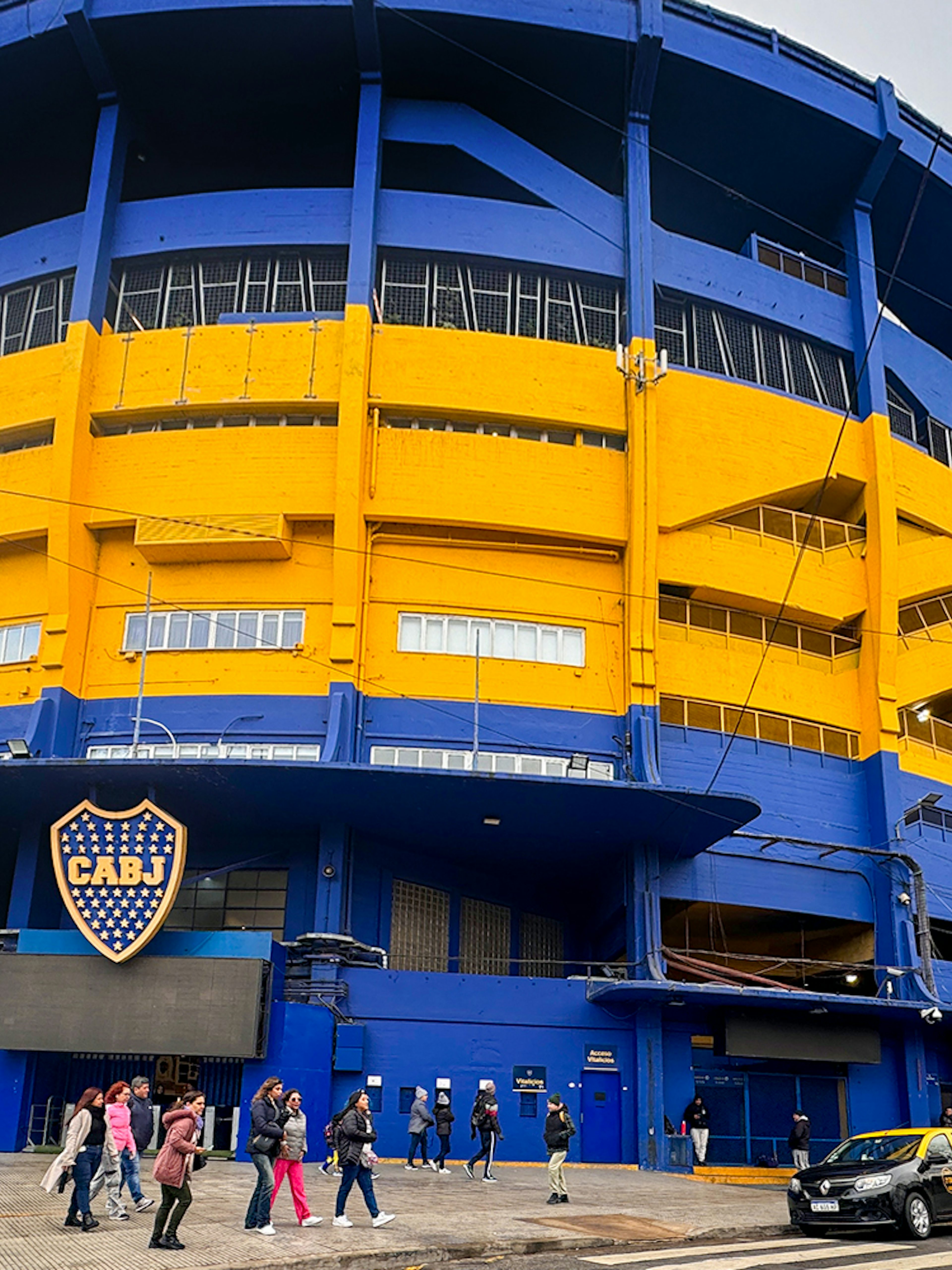 La Bombonera stadium exterior with people walking and taxis parked, Buenos Aires.