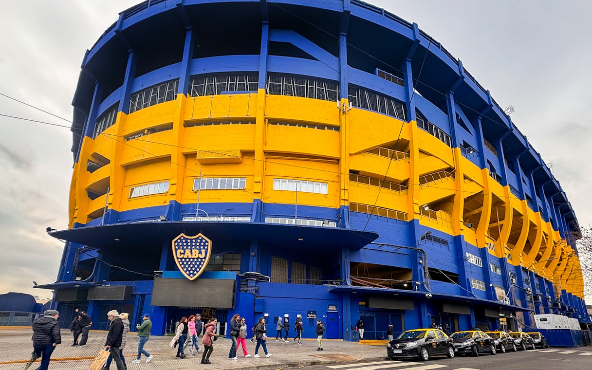 La Bombonera stadium exterior with people walking and taxis parked, Buenos Aires.
