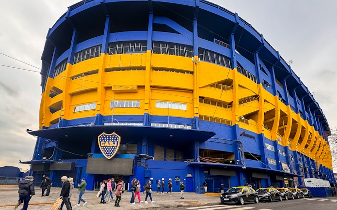 La Bombonera stadium exterior with people walking and taxis parked, Buenos Aires.