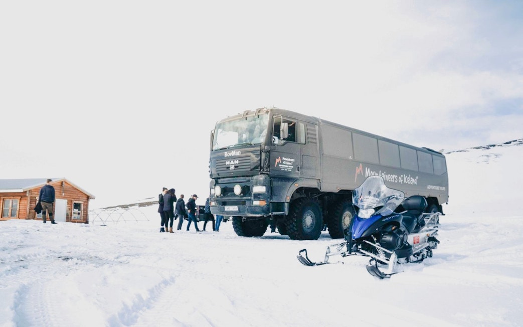 Monster truck and snowmobile on snowy terrain in Iceland with tourists nearby.