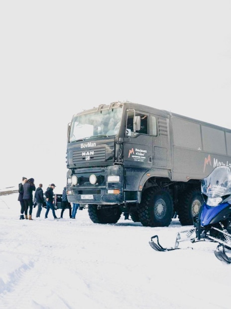 Monster truck and snowmobile on snowy terrain in Iceland with tourists nearby.