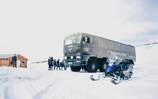 Monster truck and snowmobile on snowy terrain in Iceland with tourists nearby.