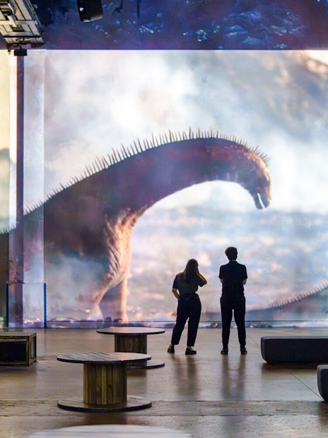 Visitors viewing dinosaur projection at Prehistoric Planet exhibition, Atelier des Lumières, Paris.