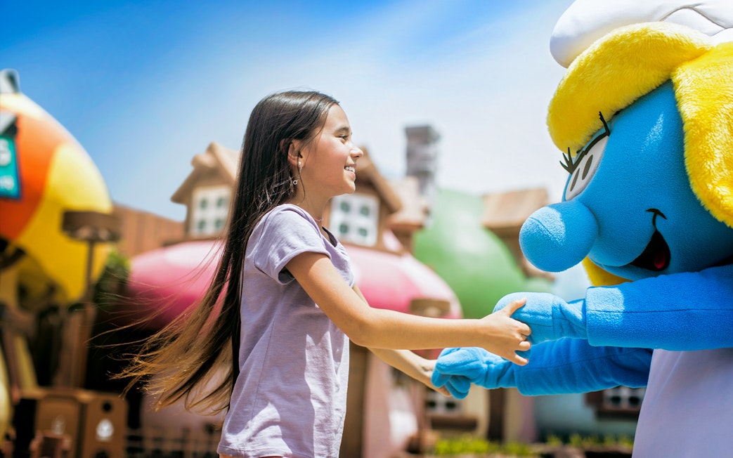 Child interacting with a blue character at a Dubai theme park.