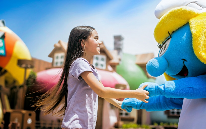 Child interacting with a blue character at a Dubai theme park.