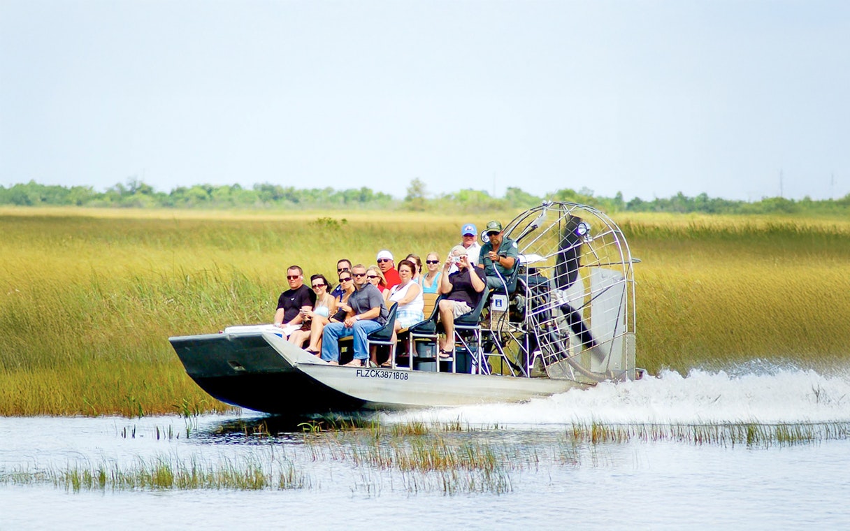 Airboat with tourists gliding through Everglades National Park wetlands.