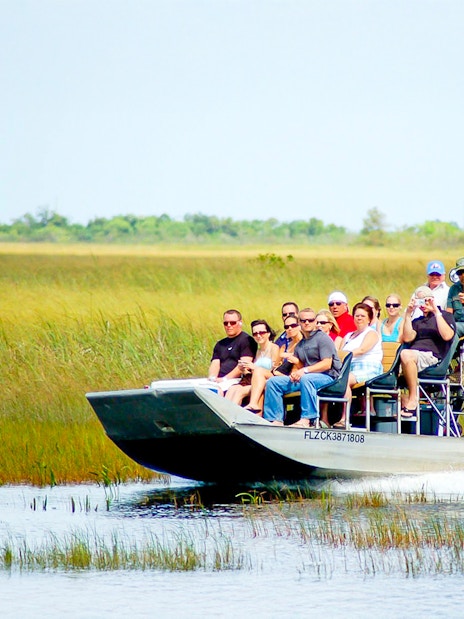 Airboat with tourists gliding through Everglades National Park wetlands.