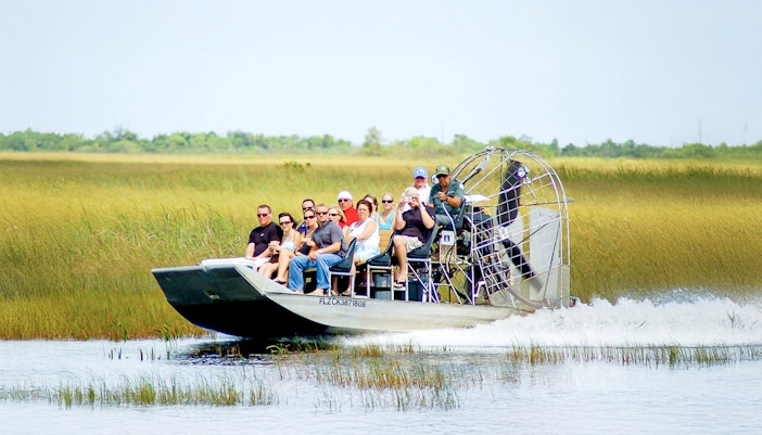 Airboat with tourists gliding through Everglades National Park wetlands.