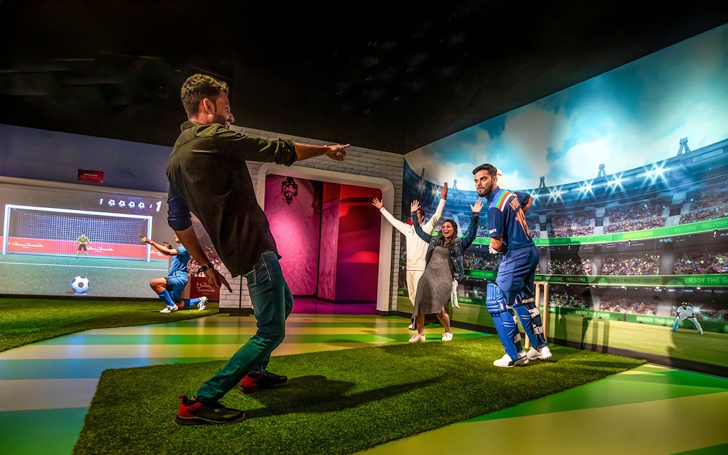 Fans posing with Virat Kohli wax figure at Madame Tussauds Dubai cricket exhibit.