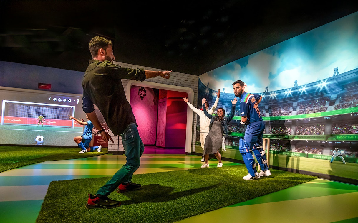 Fans posing with Virat Kohli wax figure at Madame Tussauds Dubai cricket exhibit.