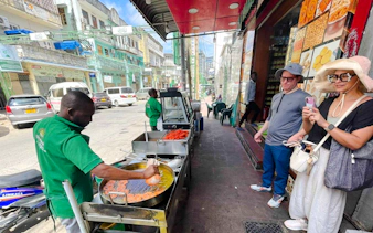 Street vendor cooking food in Zanzibar with tourists observing.
