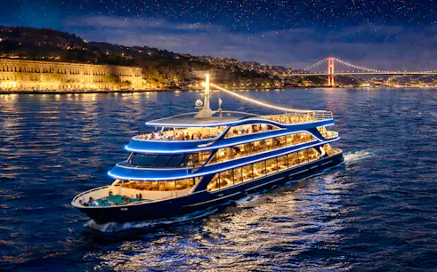 Bosphorus dinner cruise ship sailing at night with Istanbul skyline and bridge in the background.