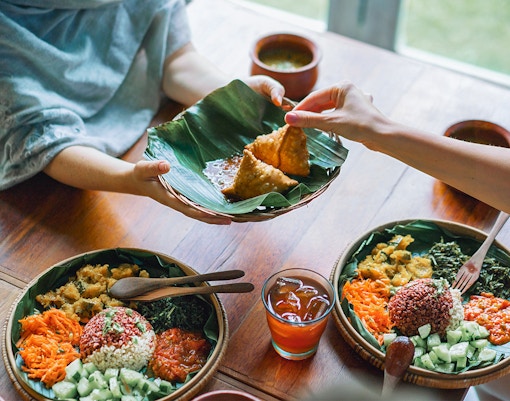 Samosas served on a banana leaf with vegan Indian dishes and iced tea on a wooden table.