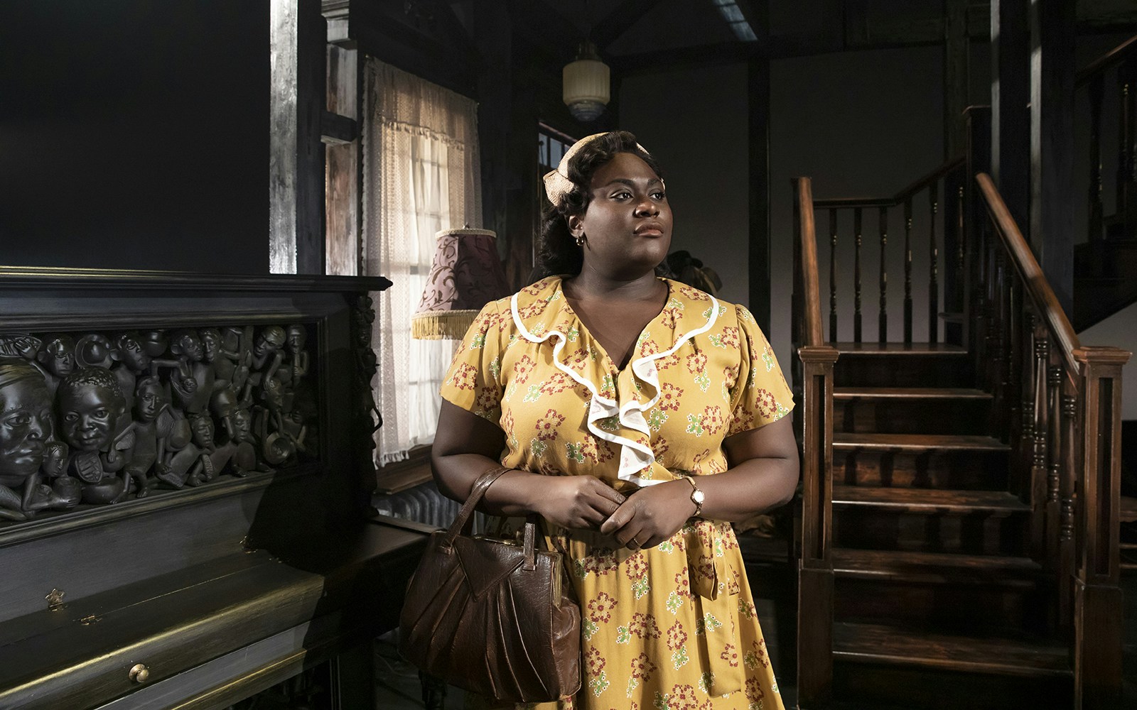 Woman standing by a carved piano in a vintage room, related to "The Piano Lesson.