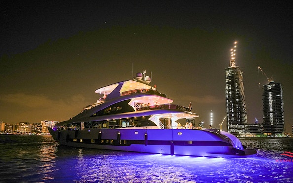 Superyacht cruising near Dubai Marina at night with city skyline in background.