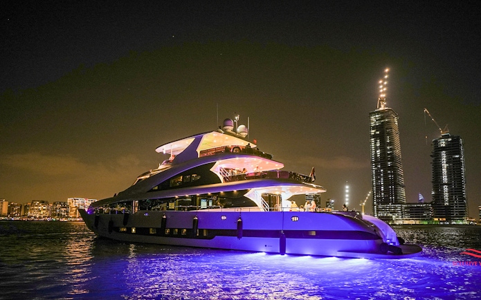 Superyacht cruising near Dubai Marina at night with city skyline in background.