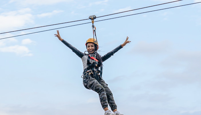 Woman ziplining at Hatta Wadi Hub, Dubai, with mountainous landscape in the background.