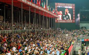 Crowd watching a rugby match at Emirates Dubai 7s stadium with flags and large screen.