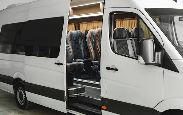 Airport transfer shuttle with open door showing passenger seats.