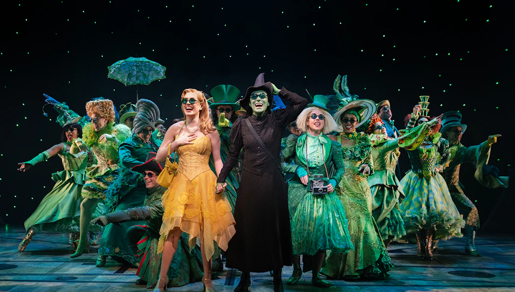 Cast of "Wicked" performing on stage in vibrant costumes.