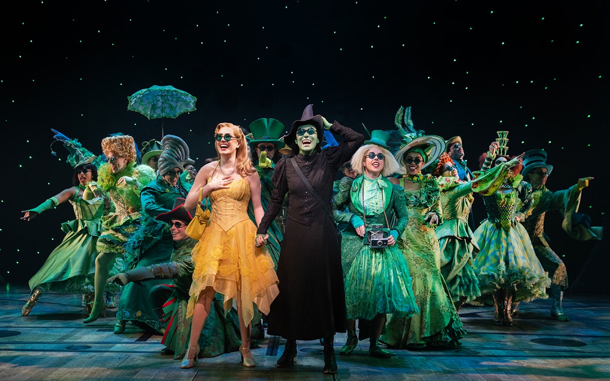 Cast of "Wicked" performing on stage in vibrant costumes.