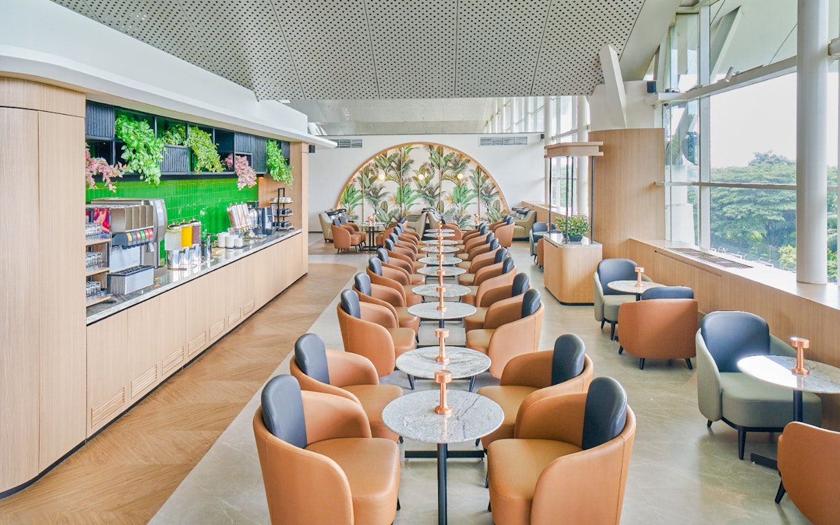 Lounge seating arrangement with rows of chairs and tables, featuring a refreshment area.