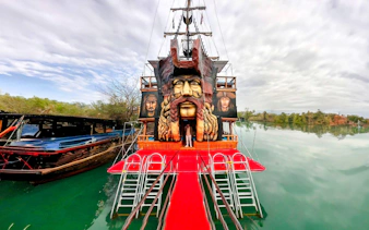Pirate ship with large face sculpture docked on a calm river, Pirate Ship Cruise.