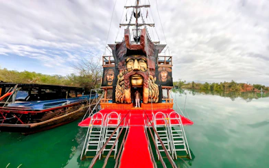 Pirate ship with large face sculpture docked on a calm river, Pirate Ship Cruise.