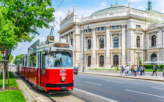 Red tram in front of Vienna's Burgtheater, Austria, with people walking nearby.