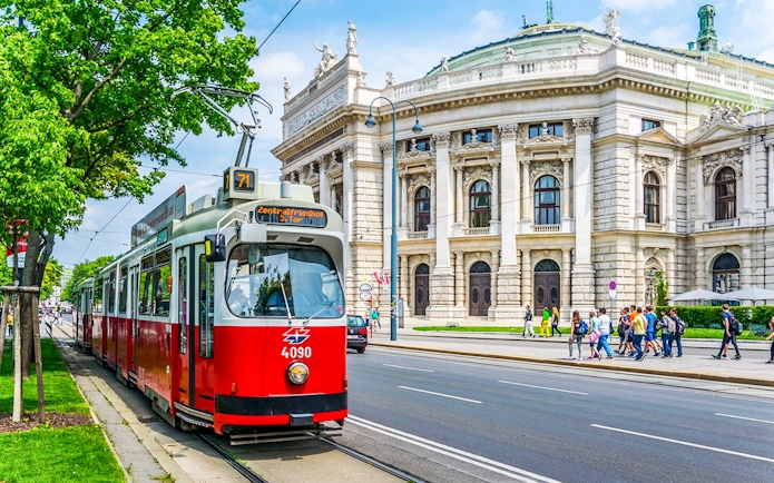 Red tram in front of Vienna's Burgtheater, Austria, with people walking nearby.