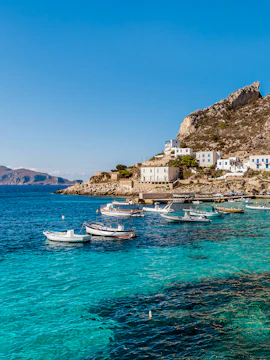 Boats anchored near rocky coastline of Egadi Islands, Italy, with clear blue water.