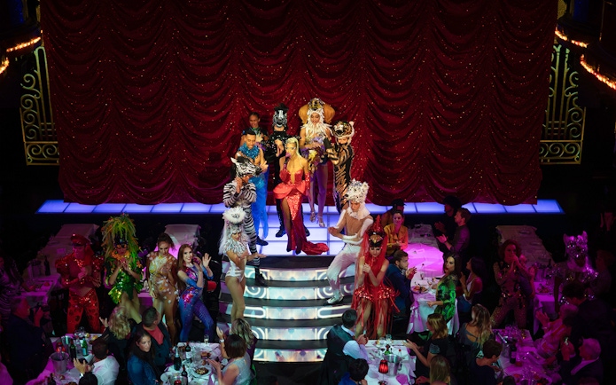 Cabaret performers on stage at Paradis Latin, Paris, with vibrant costumes and audience dining.