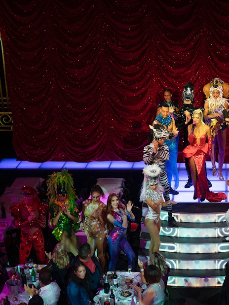 Cabaret performers on stage at Paradis Latin, Paris, with vibrant costumes and audience dining.