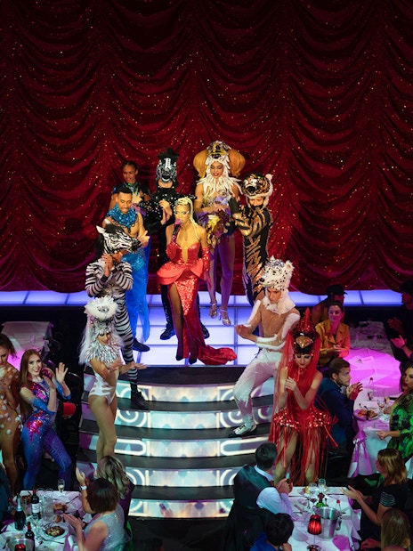 Cabaret performers on stage at Paradis Latin, Paris, with vibrant costumes and audience dining.