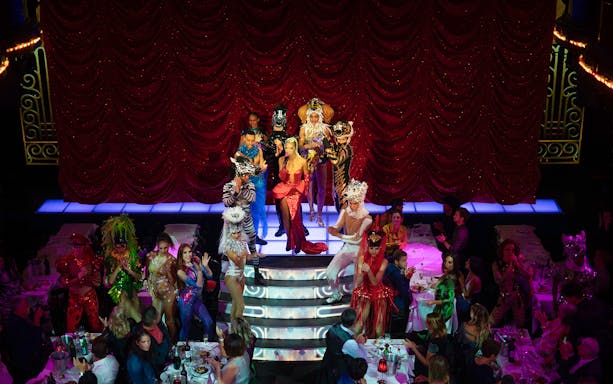 Cabaret performers on stage at Paradis Latin, Paris, with vibrant costumes and audience dining.