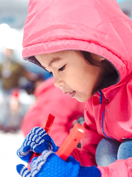 Child in red jacket playing at indoor ski park.